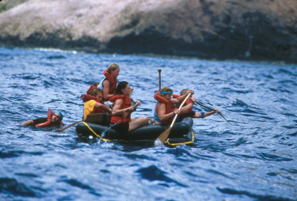 A group of people in life jackets are paddling on a raft.