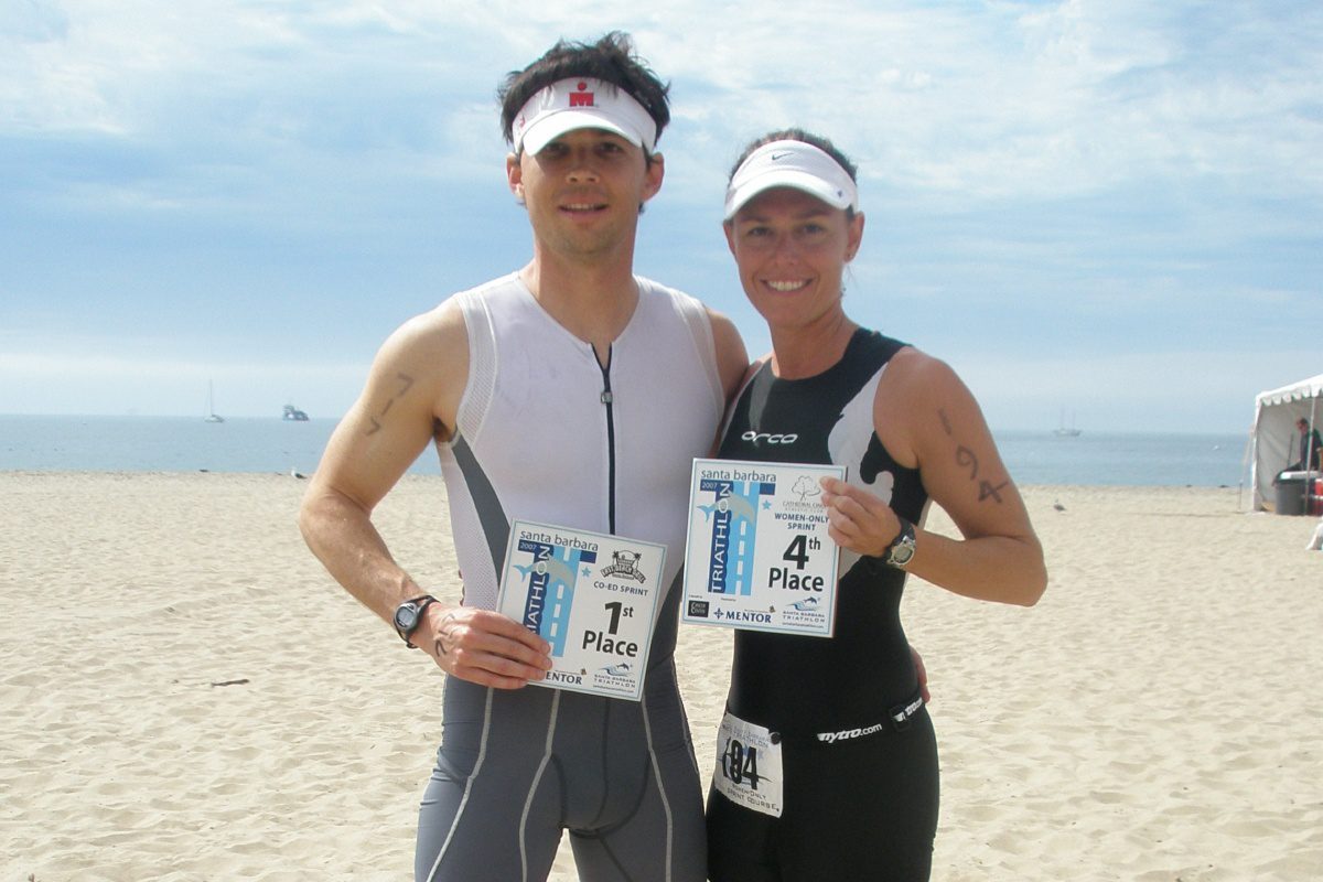 Two people standing on a beach holding up their race numbers.