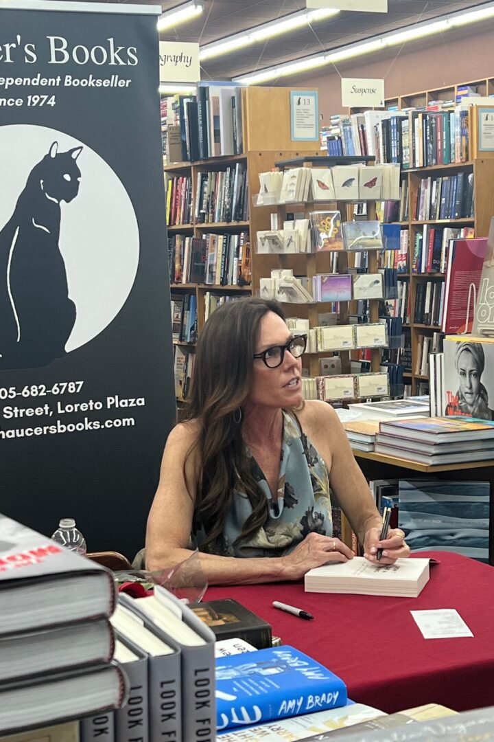 A woman sitting at a table signing a book.