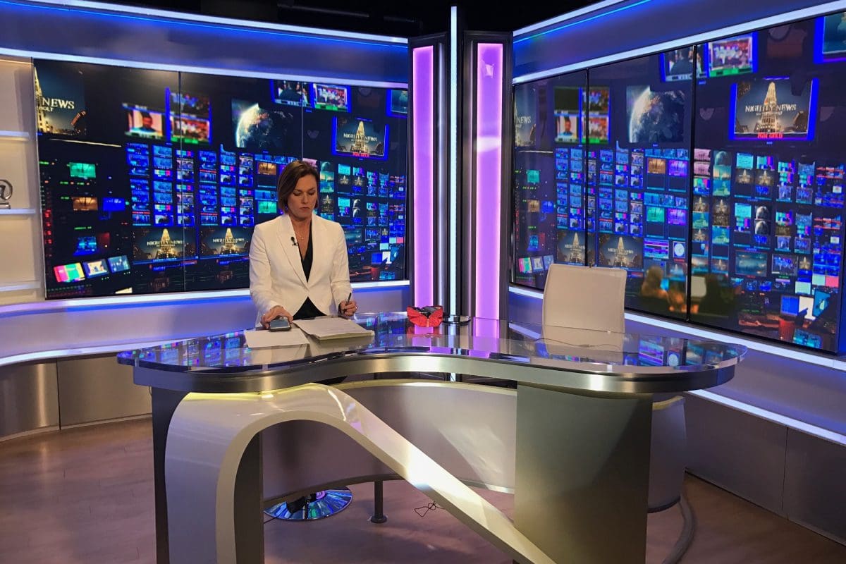 A woman sitting at the desk in front of a television.