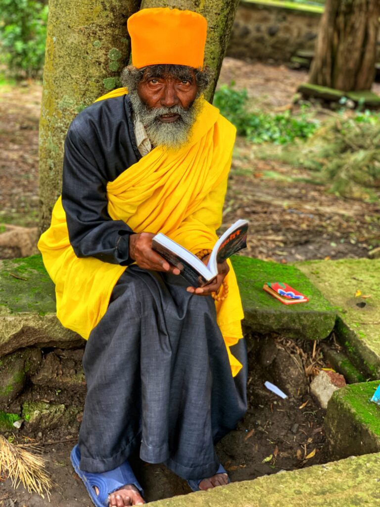 A man in yellow and black sitting on the ground reading.