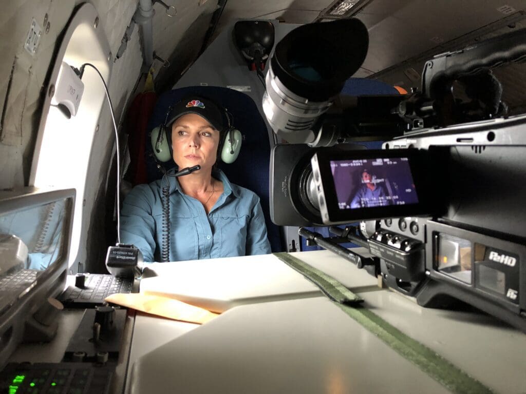 A woman in headphones and ear muffs sitting inside of an airplane.