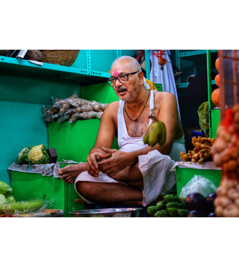 A man sitting in front of some vegetables.
